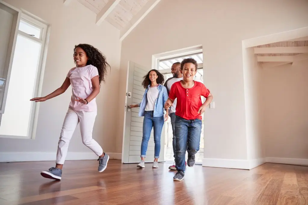 A family of four enters a new home with the two children running ahead into an empty living room.