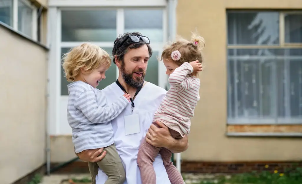 A man in a white medical uniform holding two young children.