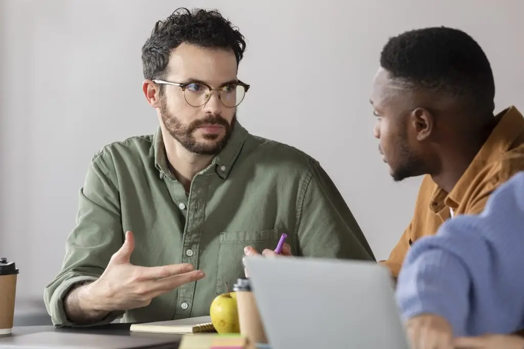 Two men in shirts sitting at a table and talking during a meeting.